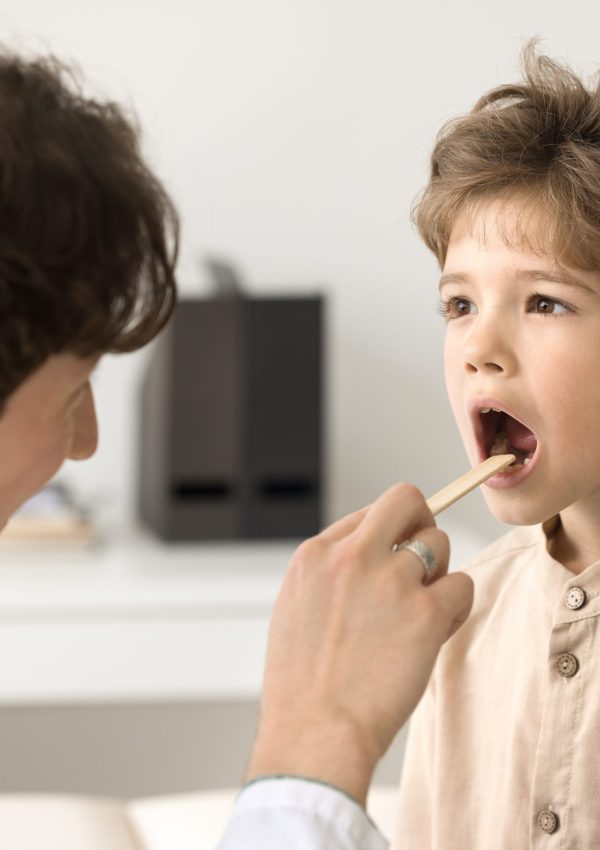 Young,Male,Pediatrician,In,Medical,Coat,Holds,Wooden,Spatula,Examining